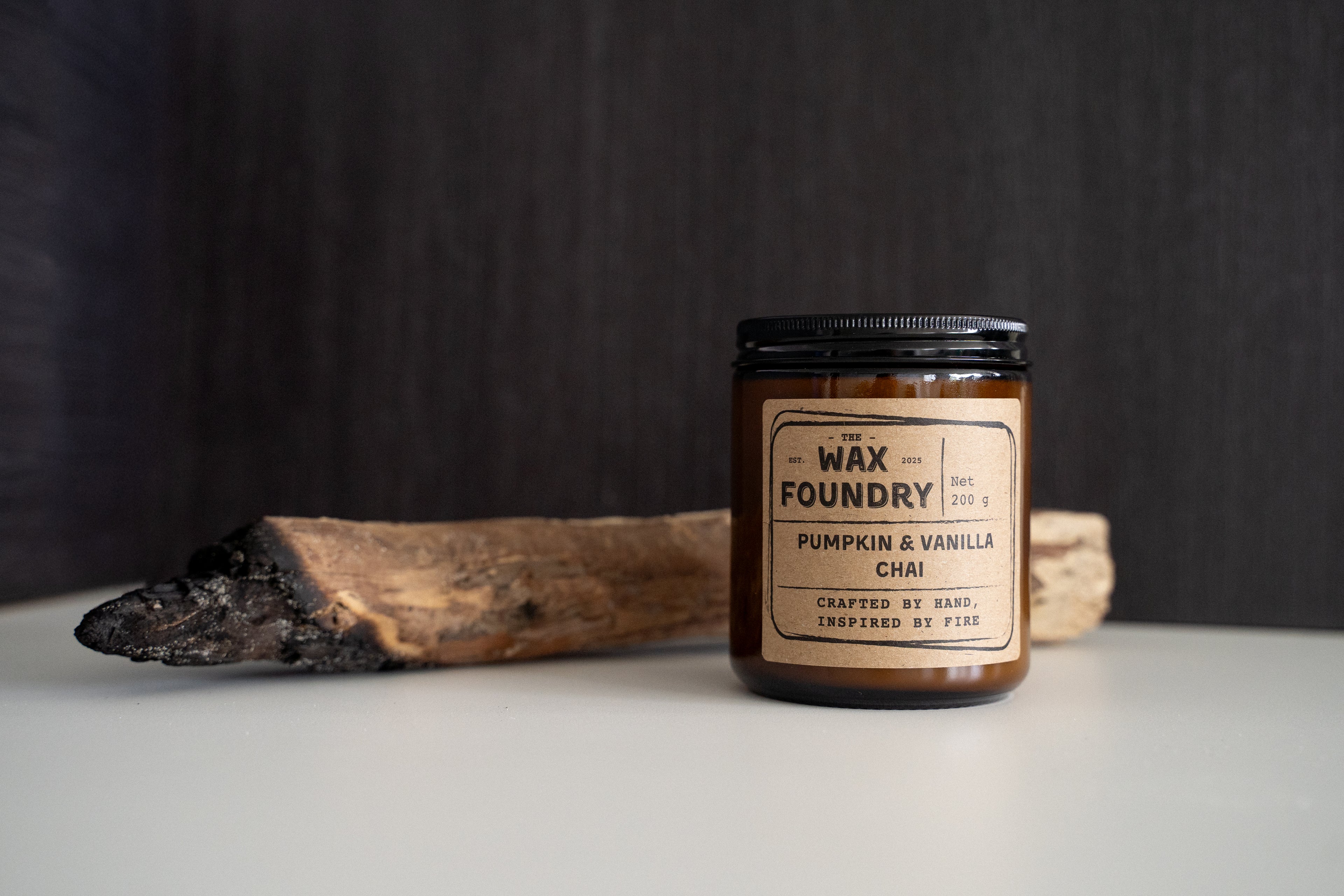 Candle labeled 'The Wax Foundry' with a wooden stick on a dark background