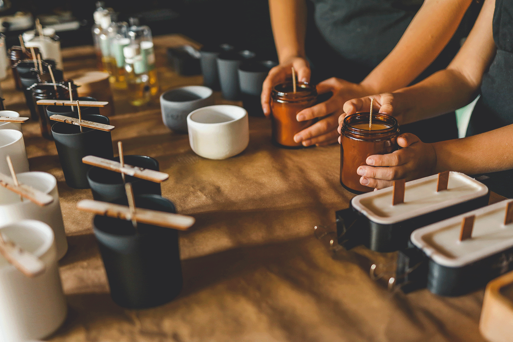 Person preparing drinks at a bar with various cups and bottles on a wooden counter.